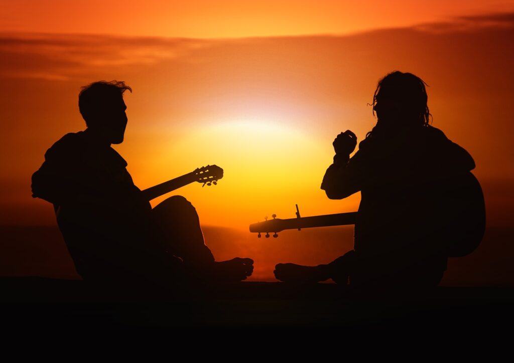 Two men playing guitar at sunrise. Bonding over music supports health and well-being.